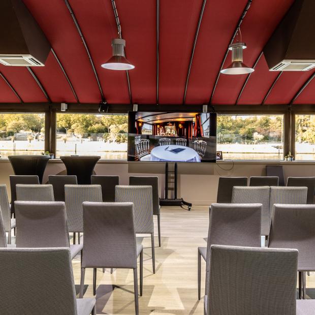 Salle de conférence sur péniche à Paris avec chaises grises et écran TV, plafond rouge
