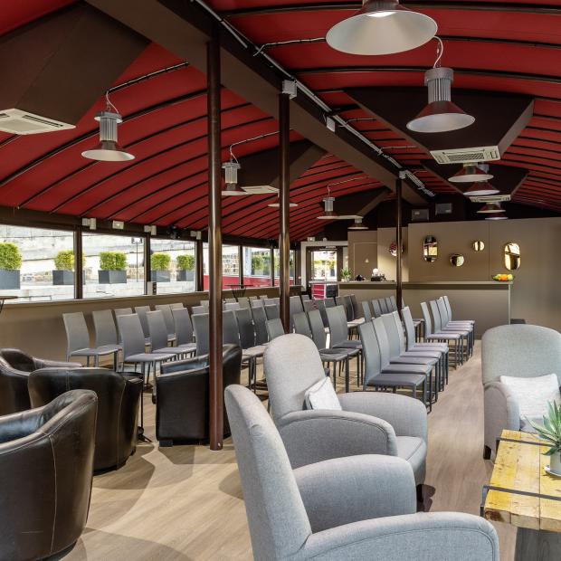 Salle événementielle sur péniche à Paris avec plafond rouge, chaises et fauteuils gris, ambiance séminaire