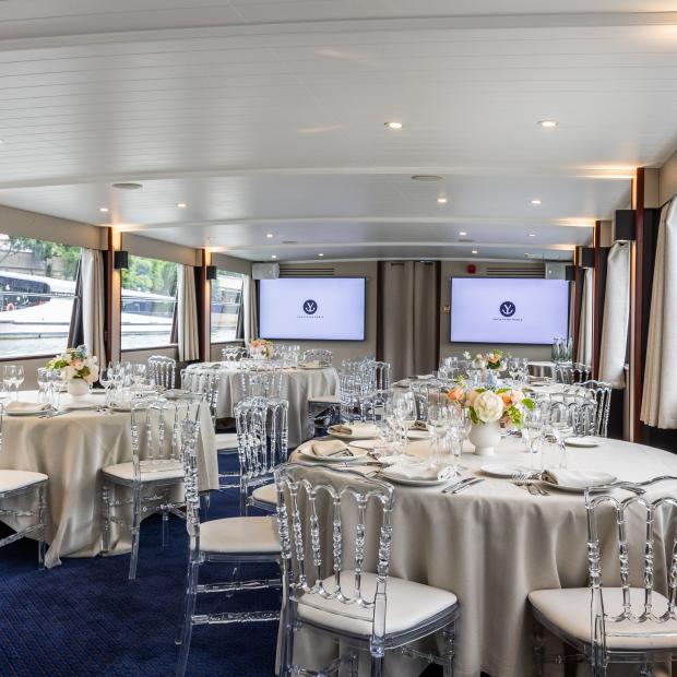 Salle de réception élégante des Yachts de Paris avec tables rondes dressées et chaises transparentes