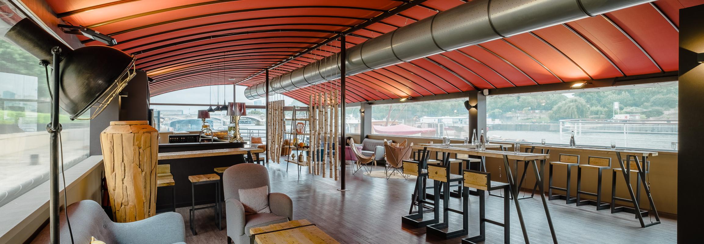 Salon lounge Atelier sur péniche avec plafond rouge, canapés gris et vue sur la rivière